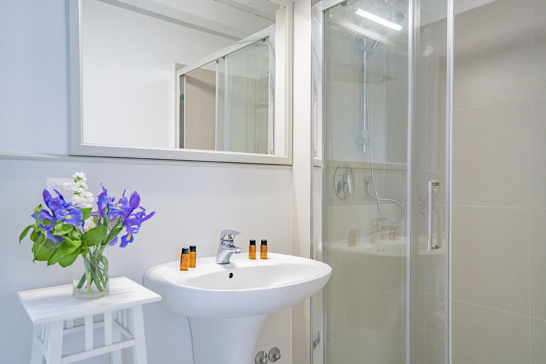 A bathroom with a white sink, mirror, and glass shower enclosure.