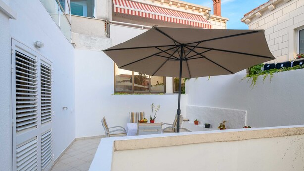 Un pequeño patio al aire libre con una mesa, sillas, un paraguas grande y plantas en macetas.