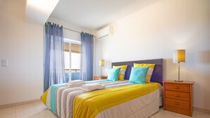Ein Schlafzimmer mit Bett, Nachttisch, Lampe und einem Fenster mit Vorhängen.