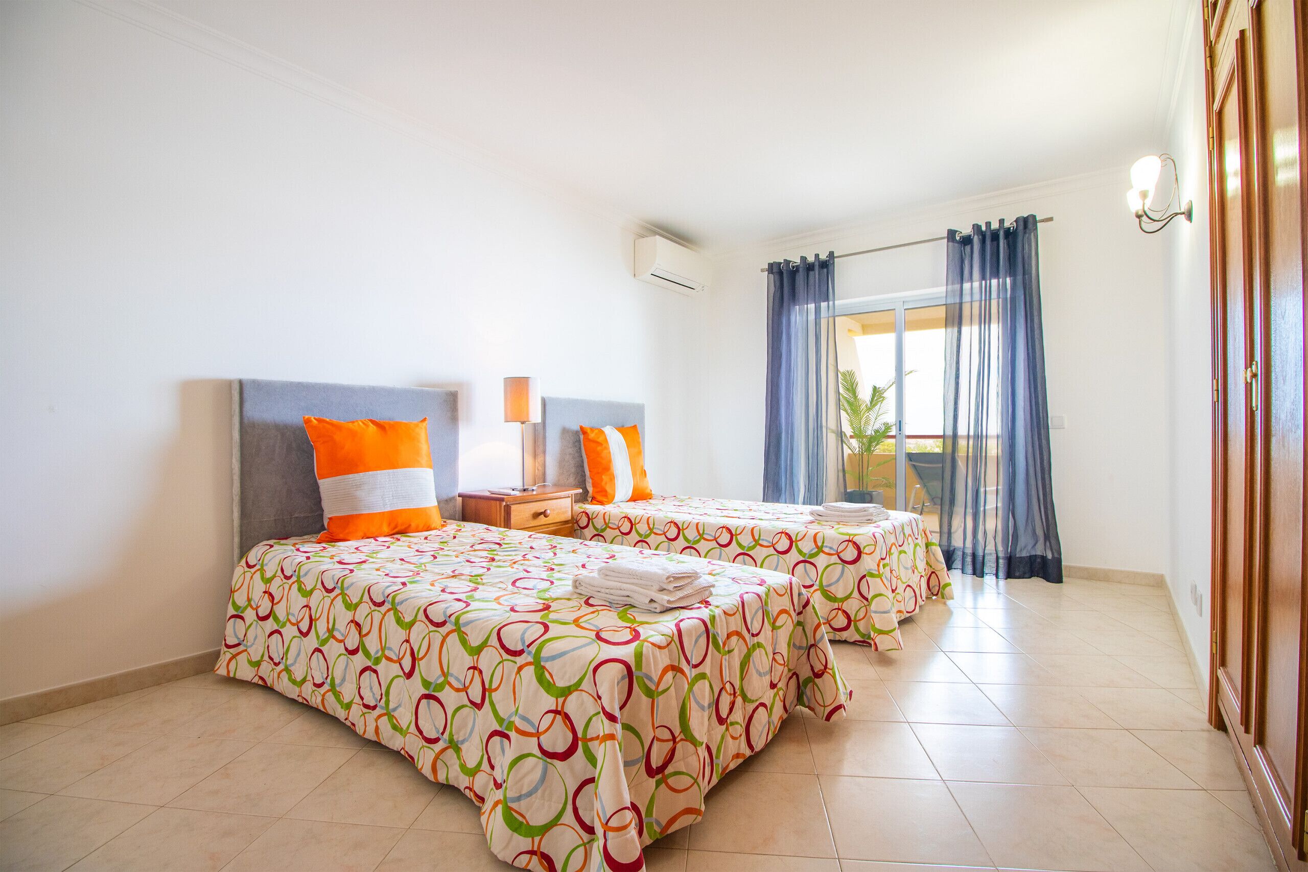 A hotel room with two beds, a nightstand, a lamp, and a window with curtains.