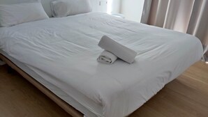 A neatly made bed with white linens and a rolled towel, a wooden headboard, and a light fixture above. - Casa Marisa, Villa CON Piscina Delante DEL MAR (Les cases de Alcanar)