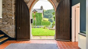 Un mur de pierre, une porte en bois, un sol carrelé et une vue sur une maison avec un jardin.