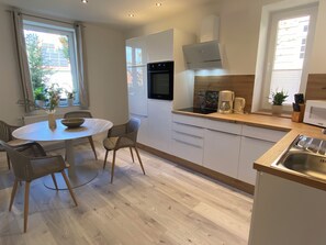 Una cocina moderna con una mesa redonda de comedor, sillas, horno empotrado, cafetera y microondas.