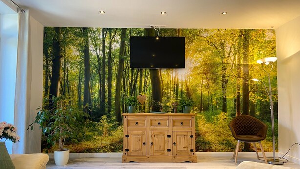 Uma sala de estar com um grande mural de floresta, um armário de madeira, um sofá, uma mesa de centro e uma poltrona.