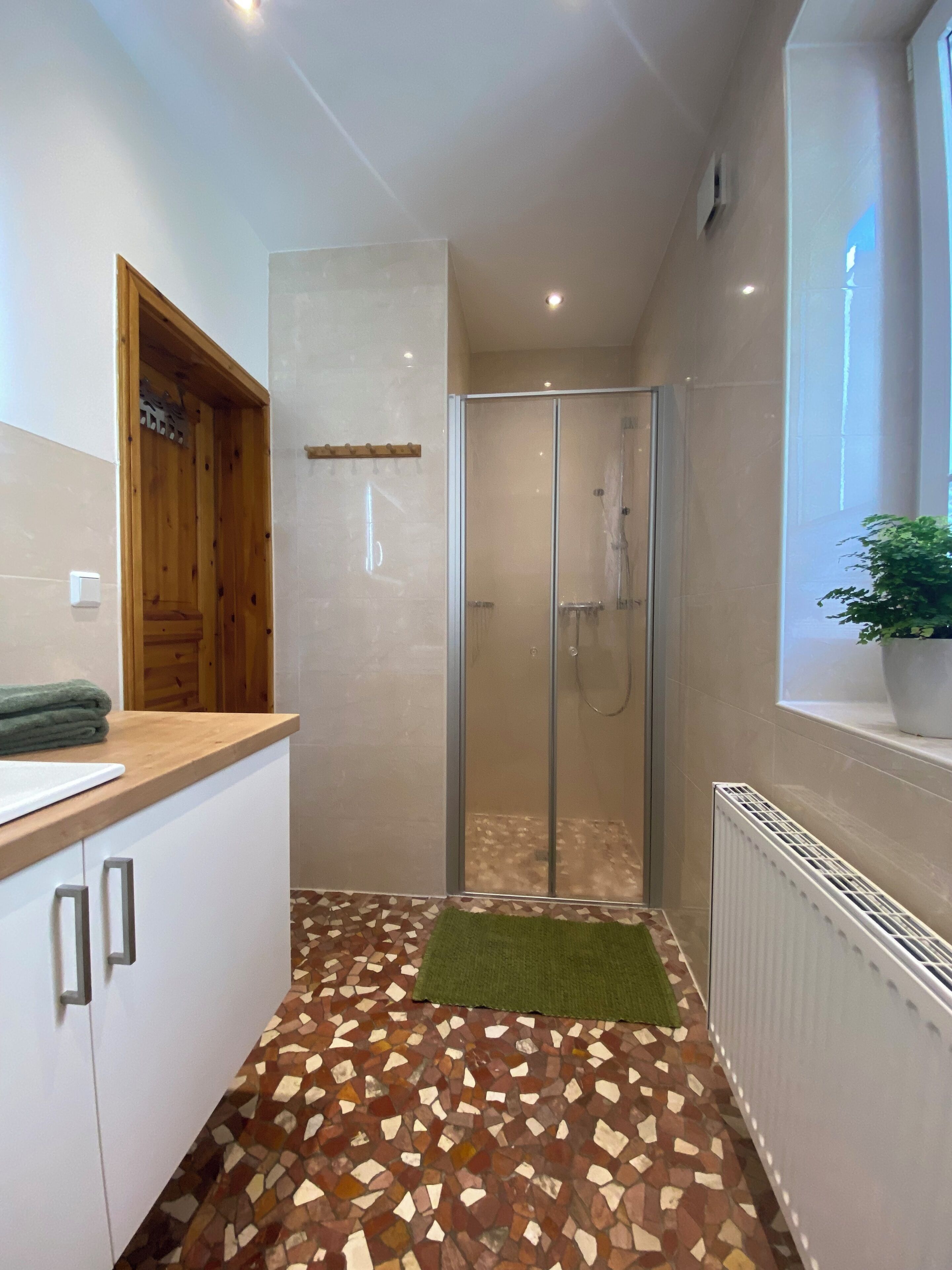 Uma casa de banho com chuveiro, um armário de madeira, chão em mosaico e radiador.
