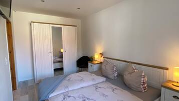 A bedroom with a bed, bedside tables, a nightstand, a desk, a chair, and a wardrobe.