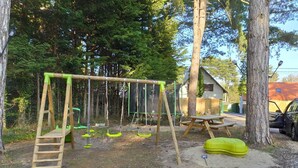 A playground with swings and a ladder, surrounded by trees and a house in the background. - Near-sea rental (Quend)
