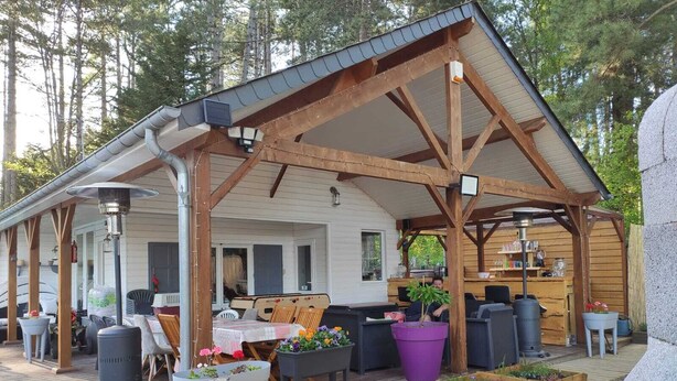 A covered outdoor area with wooden beams, a table with chairs, and potted plants. - Near-sea rental (Quend)
