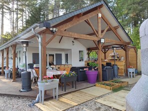 A covered outdoor area with wooden beams, a table with chairs, and potted plants. - Near-sea rental (Quend)