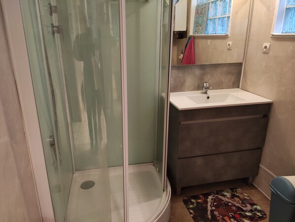 A bathroom with a glass-enclosed shower, a white sink, and a dark-colored cabinet.