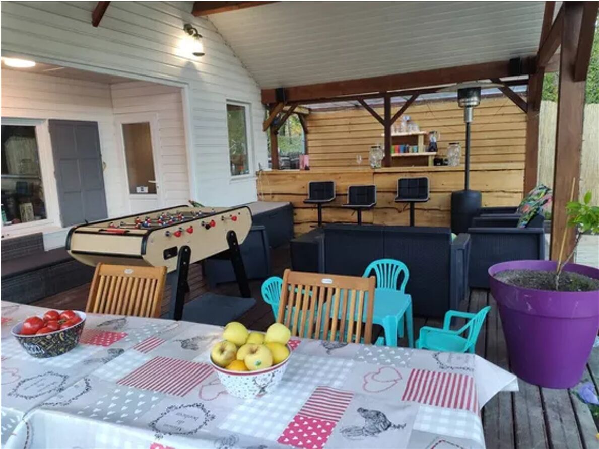 An outdoor covered patio area with a pool table, chairs, and a table with fruit and a bowl.