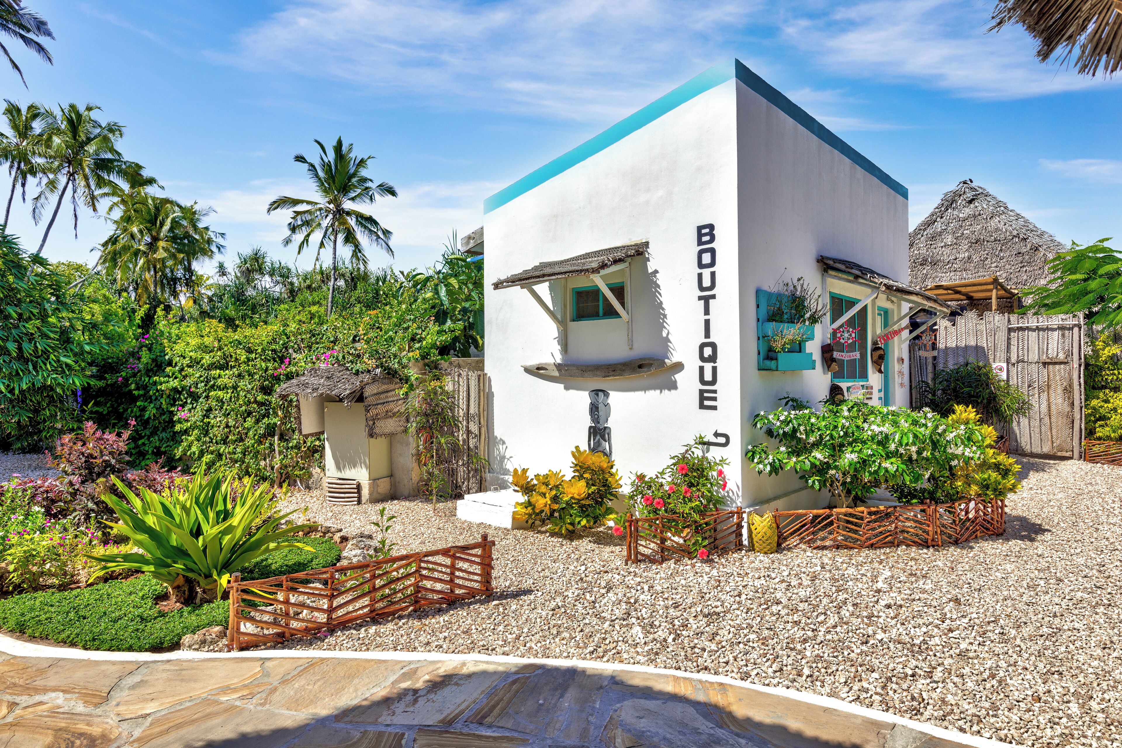 A boutique hotel with a white exterior, a thatched roof, and lush tropical landscaping.