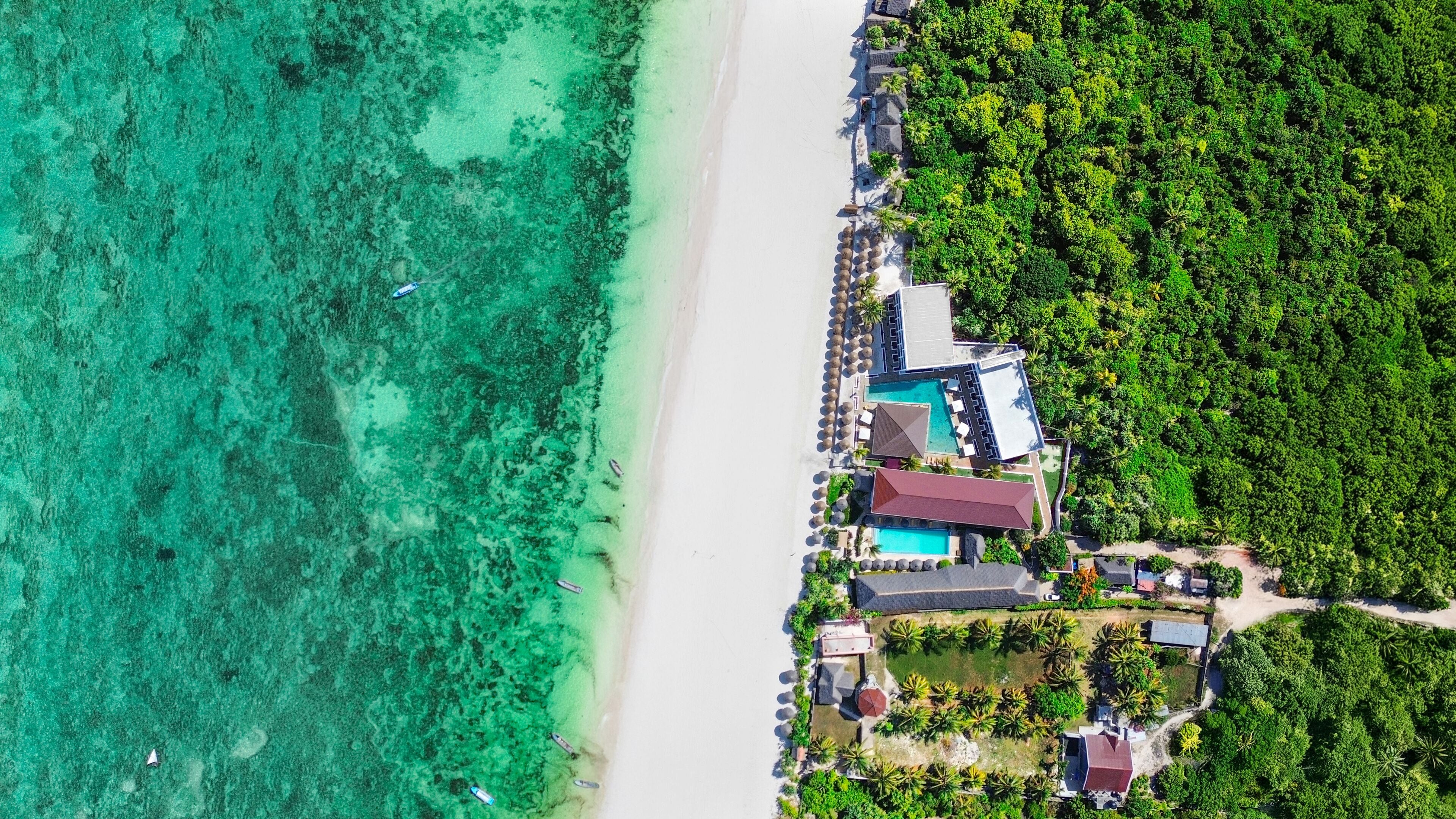 An aerial view of a coastal resort with a beach, clear turquoise waters, and lush greenery.