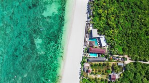 An aerial view of a coastal resort with a beach, clear turquoise waters, and lush greenery. - AHG Sun Bay Mlilile Beach Hotel (Matemwe)