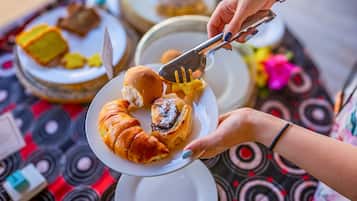 Una persona sirve comida de un plato con unas pinzas, con un mantel estampado y otros platos al fondo.