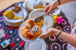 Una persona sirve comida de un plato con unas pinzas, con un mantel estampado y otros platos al fondo.