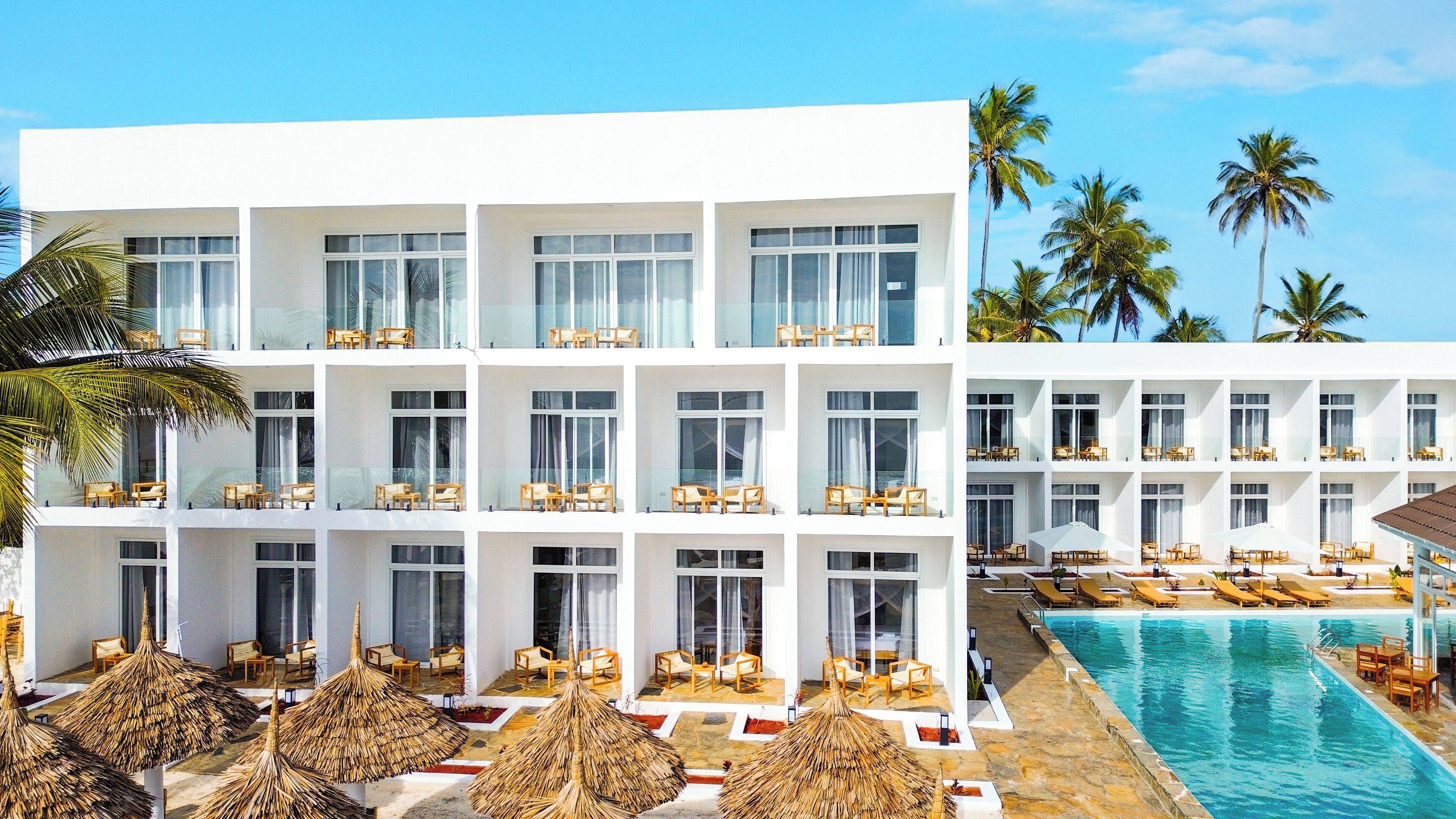 Un hotel moderno con varios balcones, piscina y palmeras.