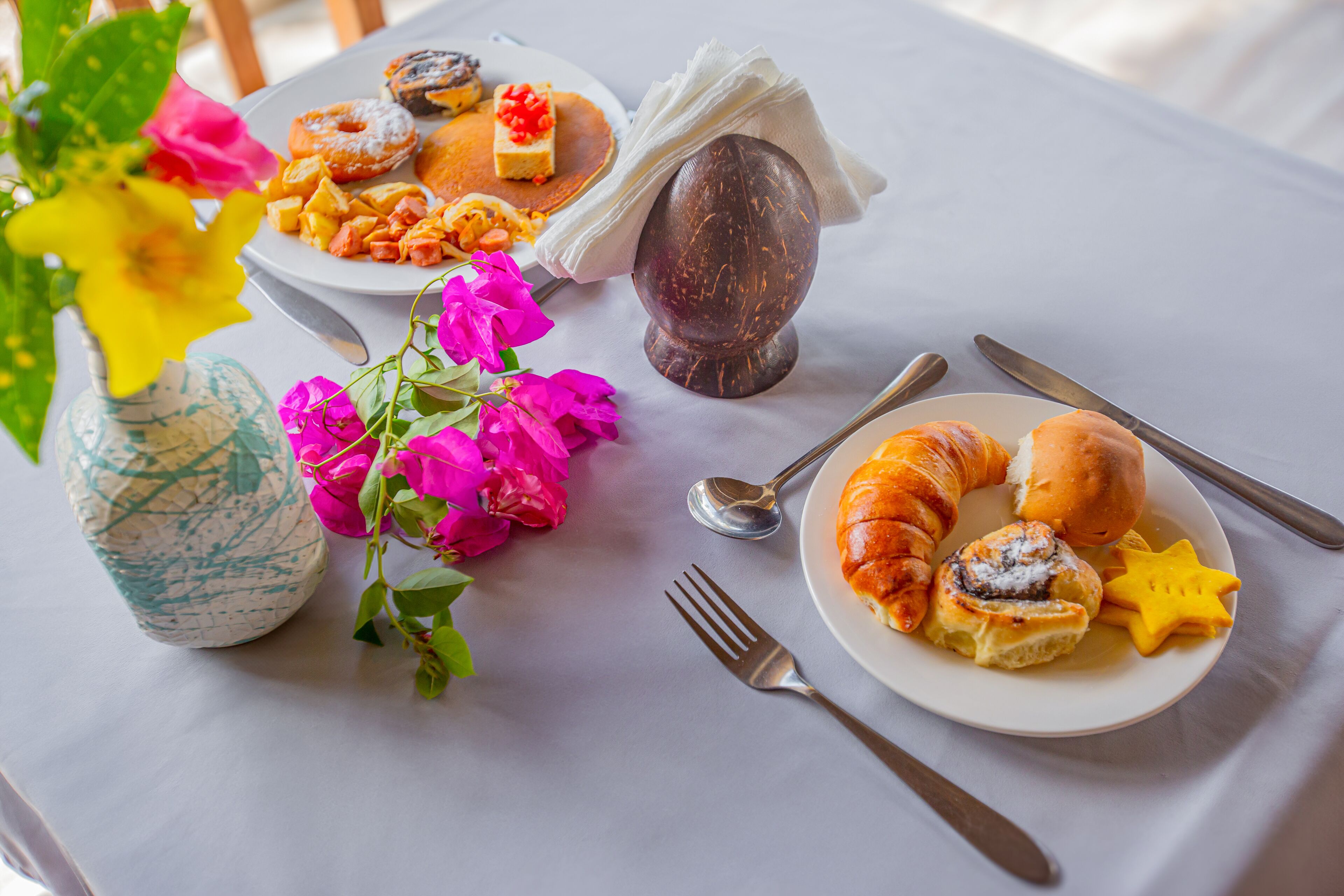 A dining table with plates of pastries, a vase with flowers, and cutlery.
