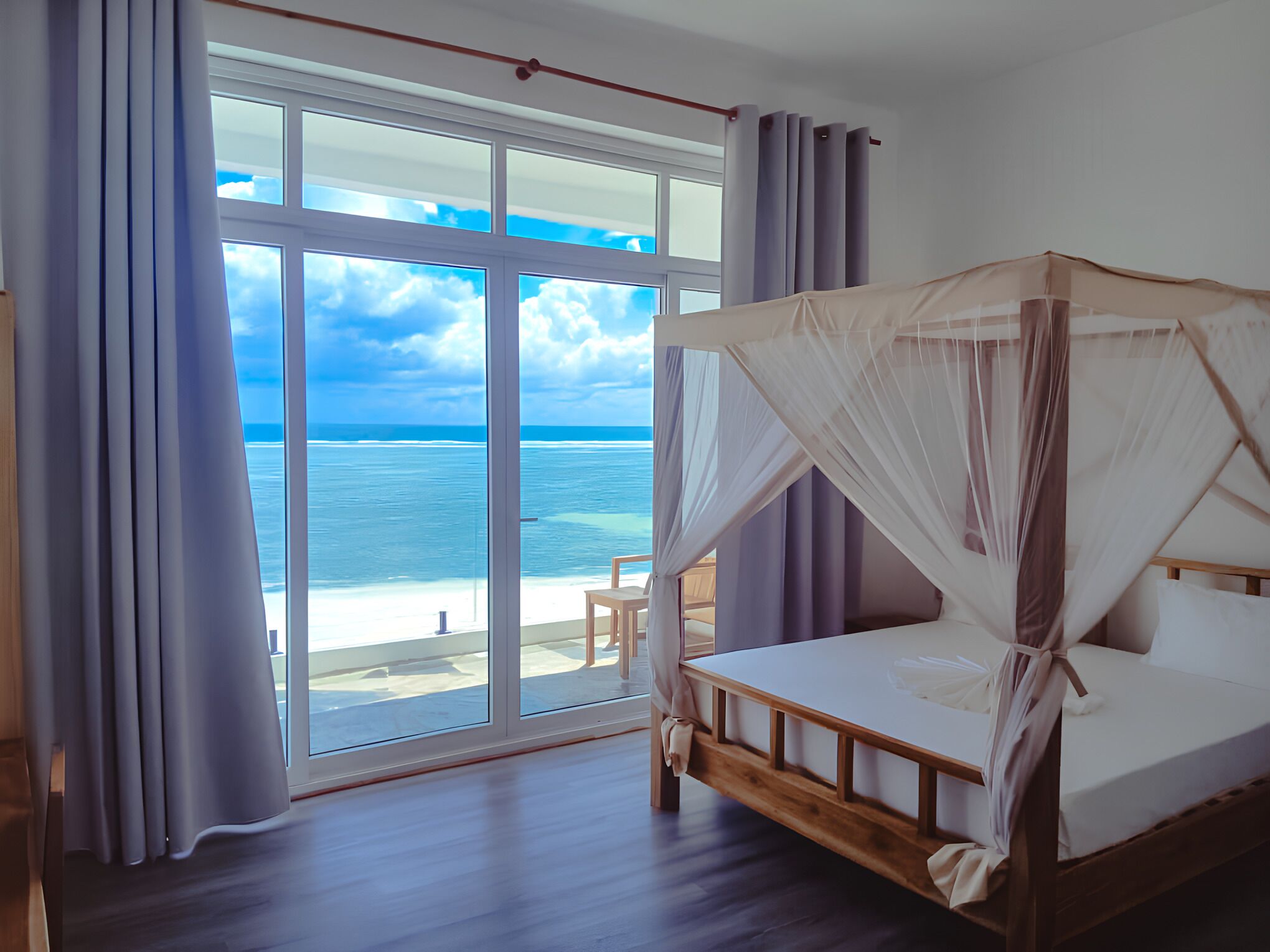 A bedroom with a wooden bed, a large window, and a view of the ocean.