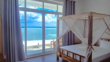 A bedroom with a wooden bed, a large window, and a view of the ocean.