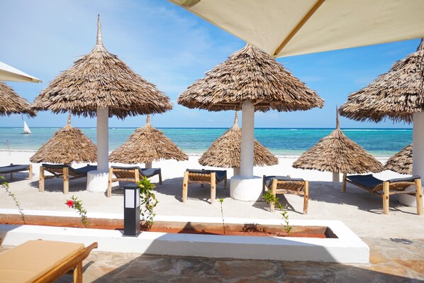 Un salón junto a la playa con sombrillas de paja y sillones de madera.