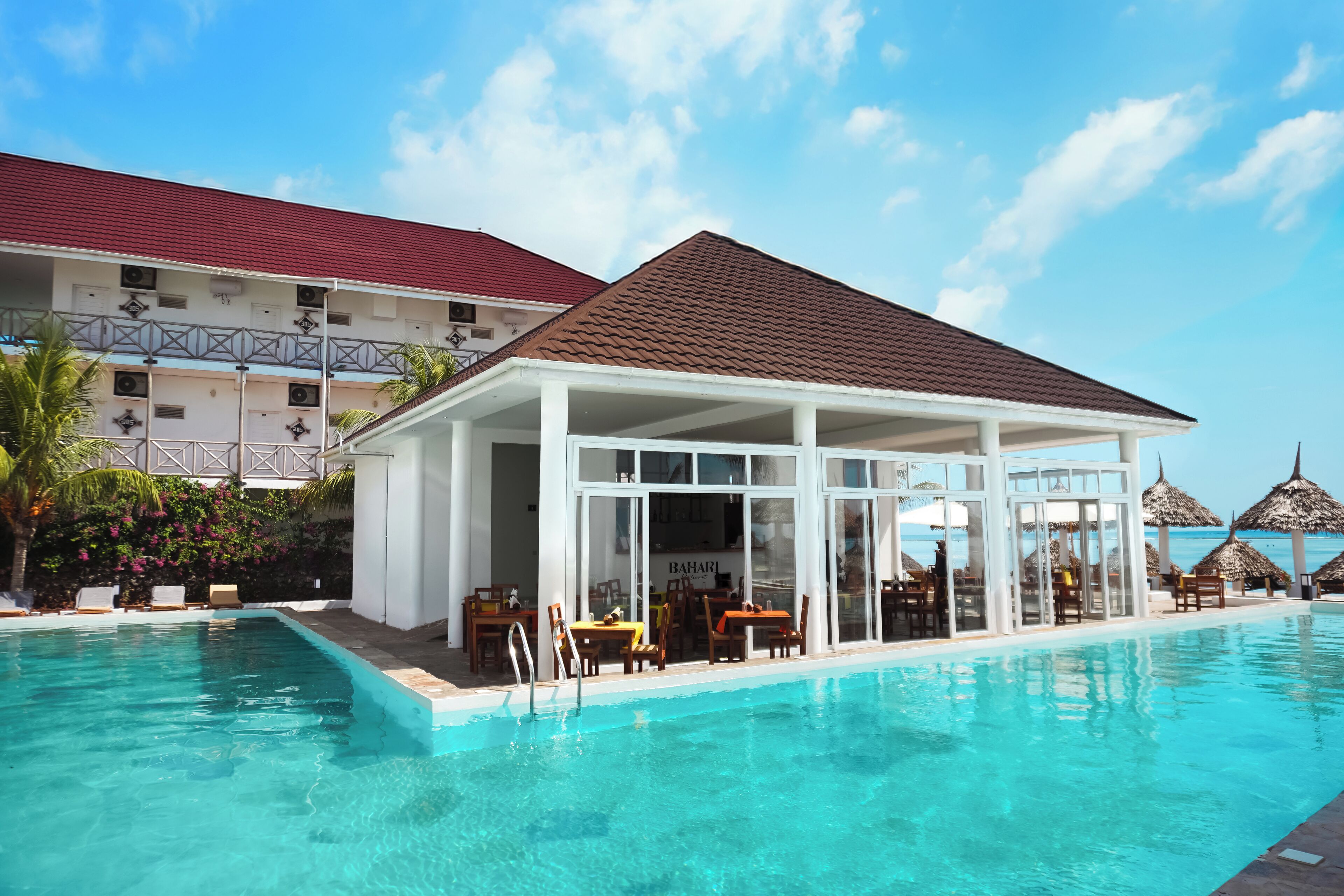 A poolside area with a covered seating area, a restaurant, and a view of the ocean.