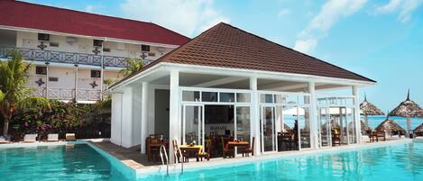 A poolside area with a covered seating area, a restaurant, and a view of the ocean.