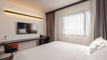 Ein Hotelzimmer mit Bett, Schreibtisch mit Stuhl, Flachbildfernseher und einem Fenster mit Vorhängen.