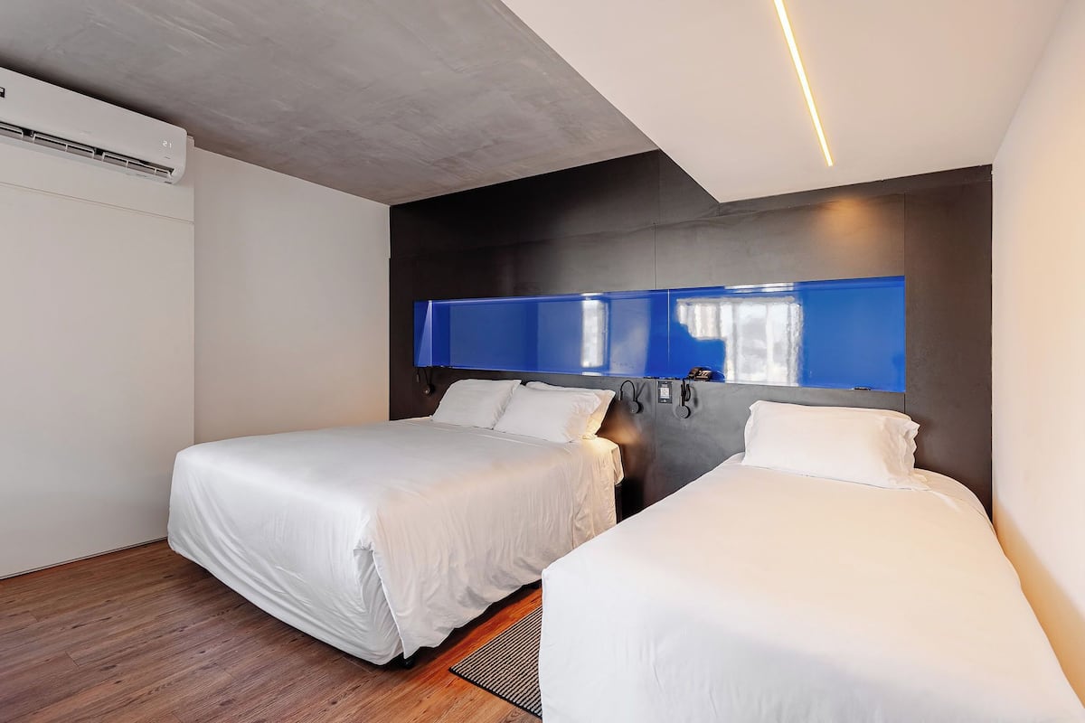 A hotel room with two beds, a modern design, a large mirror, and a ceiling air conditioner.