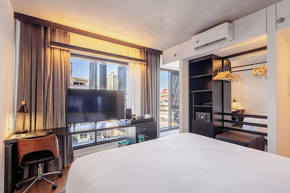 Une chambre d’hôtel avec un grand lit, un bureau avec une chaise, une télévision, une armoire et une vue sur le paysage urbain.