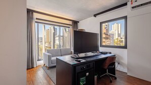 Habitación de hotel moderna con un gran ventanal, televisor de pantalla plana, escritorio con silla y sofá.
