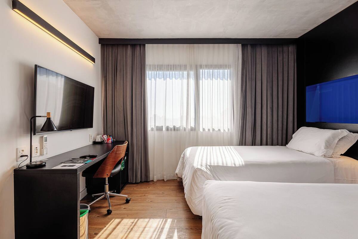 A hotel room with a bed, desk, chair, TV, and curtains.