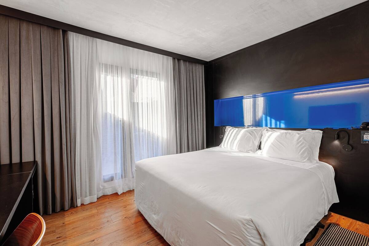 A hotel room with a large bed, a desk, a chair, and a TV mounted on the wall.