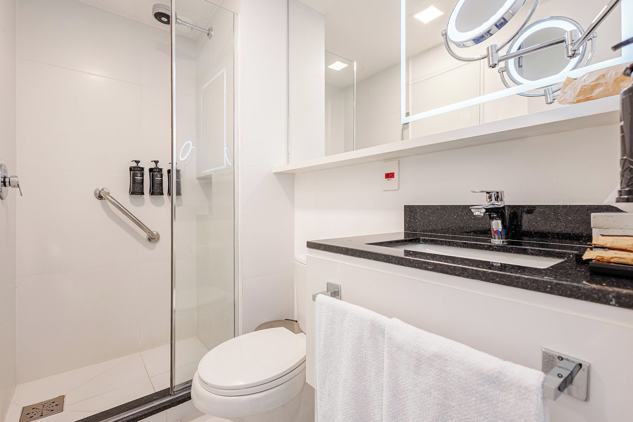 A modern bathroom with a glass shower enclosure, a white toilet, a vanity with a black countertop, and a towel rack.