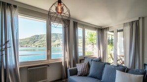 Een kamer met uitzicht op een meer en heuvels, een bank met kussens en een bijzondere geometrische lamp.