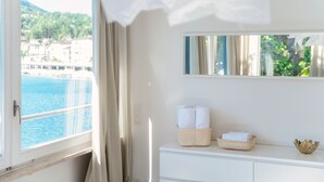 Een hotelkamer met een groot raam, een witte kaptafel met spiegel en uitzicht op zee en gebouwen.
