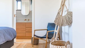 A bedroom with a bed, wooden floor, a chair, a hanging macrame bag, and a small woven basket.