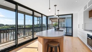 A modern kitchen with a large island, a view of the outdoors, and a balcony.