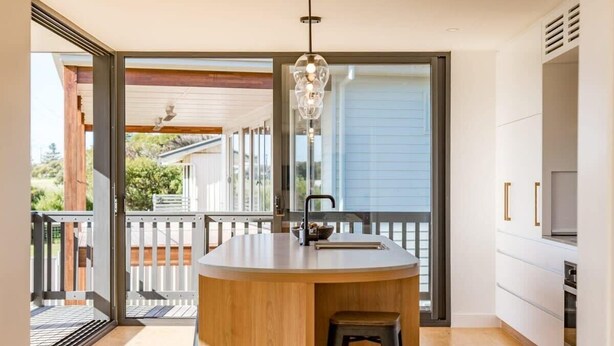 A modern kitchen with a central island, a hanging light fixture, and a sliding glass door leading to an outdoor area.