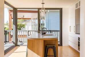 Une cuisine moderne dotée d’un îlot central, d’un luminaire suspendu et d’une porte-fenêtre coulissante donnant sur un espace extérieur.