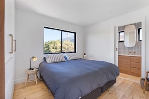 Une chambre avec un grand lit, une fenêtre, une salle de bain avec un miroir et un plancher en bois.