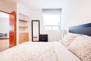 A bedroom with a bed, a dresser, a mirror, a window, and a desk.