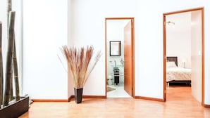 A hallway with a wooden floor, a bamboo plant, and a room with a bed and a nightstand. - Upscale Polanco | Steps to Metro, Dining & Parks (Ciudad de México)