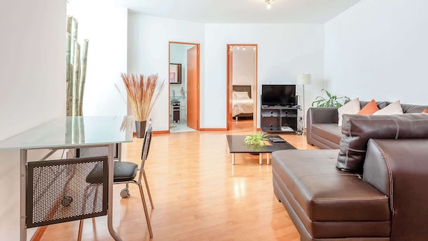 A modern living room with a glass dining table, a brown leather sofa, a TV, and a plant. - Upscale Polanco | Steps to Metro, Dining & Parks (Ciudad de México)