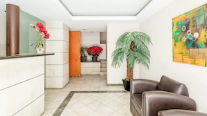 A lobby with a reception desk, a brown leather sofa, a large potted plant, and a colorful abstract painting on the wall. - Upscale Polanco | Steps to Metro, Dining & Parks (Ciudad de México)