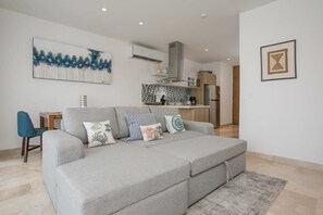 A modern living room with a grey sofa, a blue chair, and a kitchen in the background.