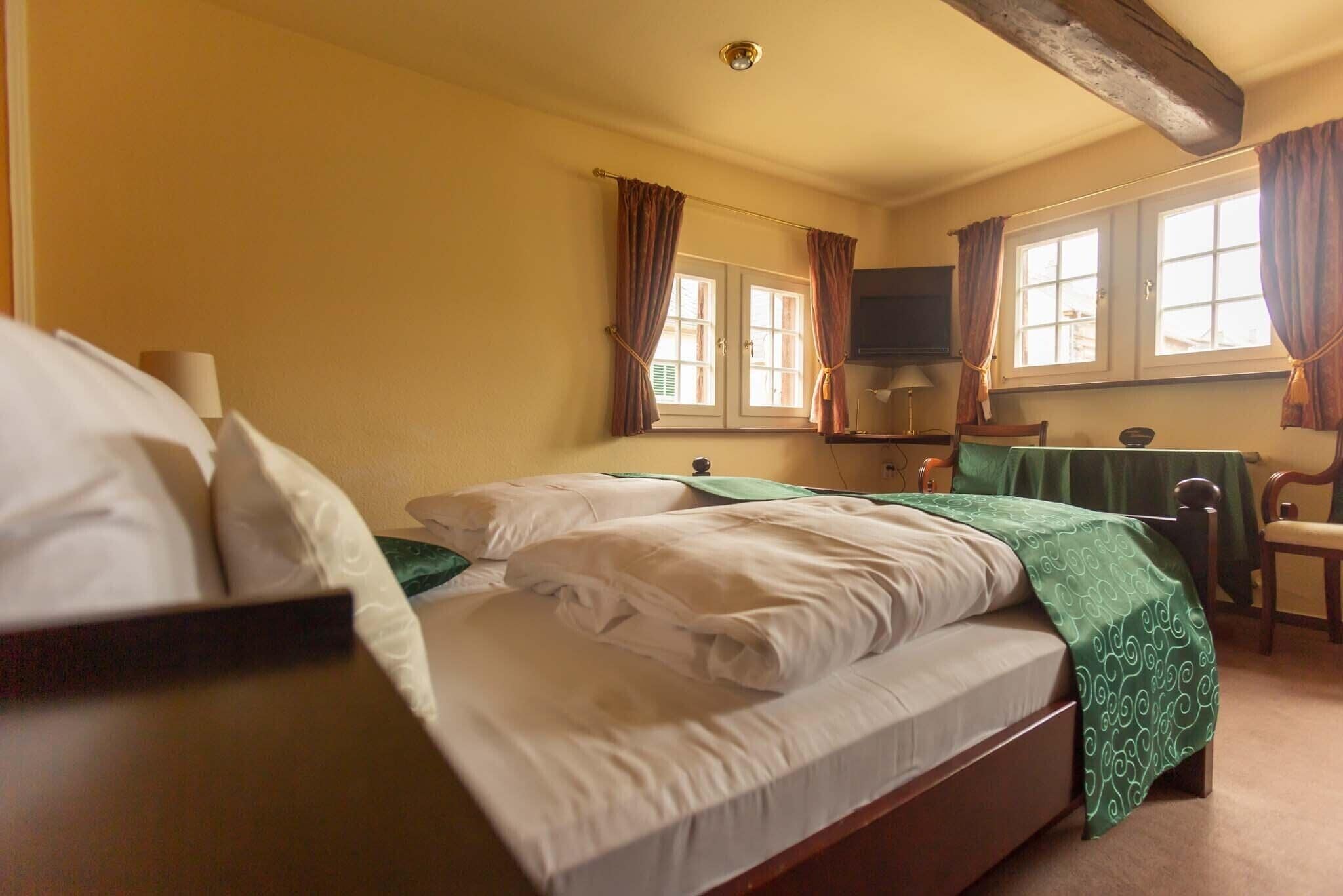 A bedroom with a bed, a chair, a table, and a window with curtains.