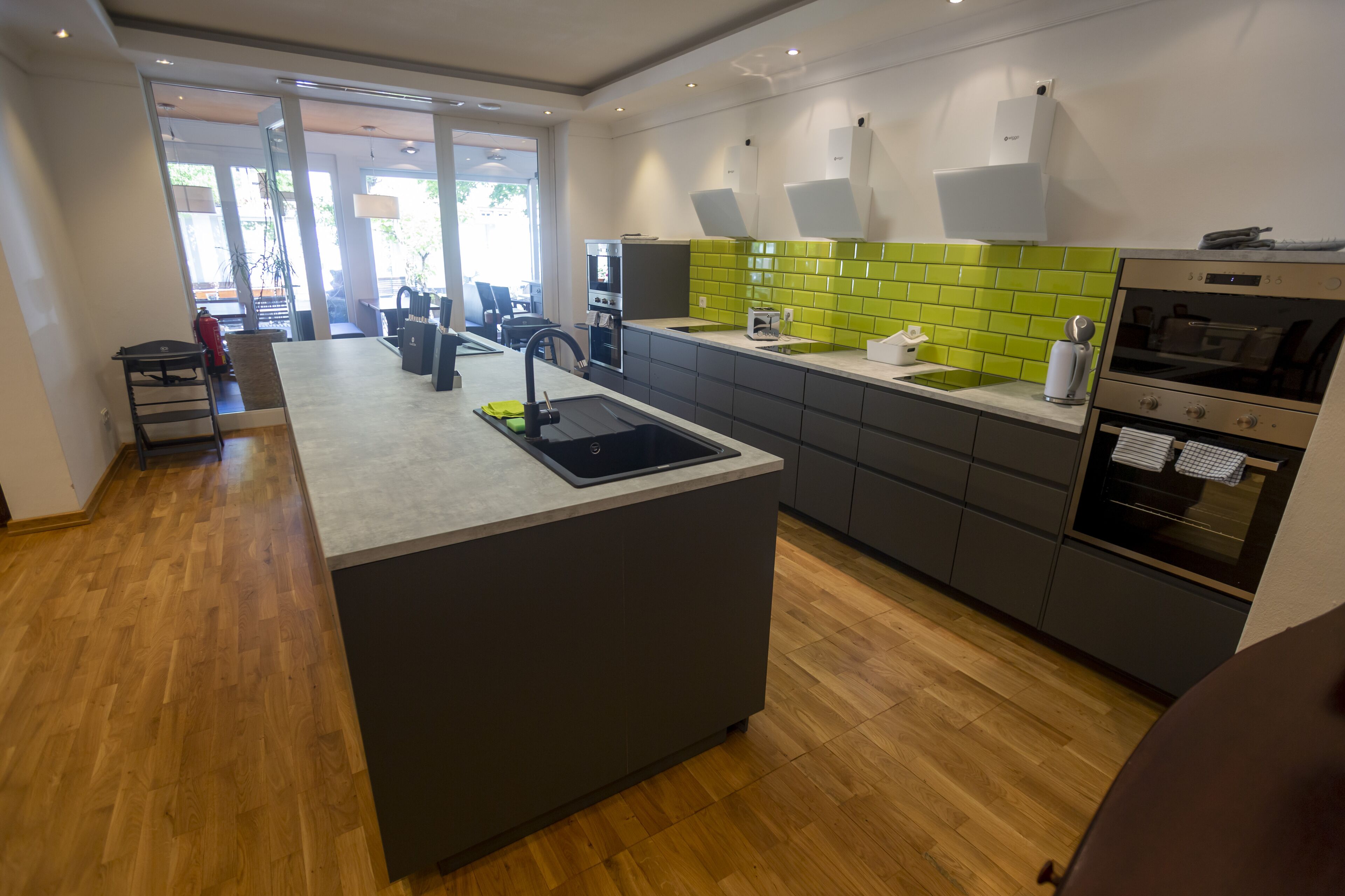 Una cocina moderna con una isla central, electrodomésticos integrados y un salpicadero de color verde brillante.