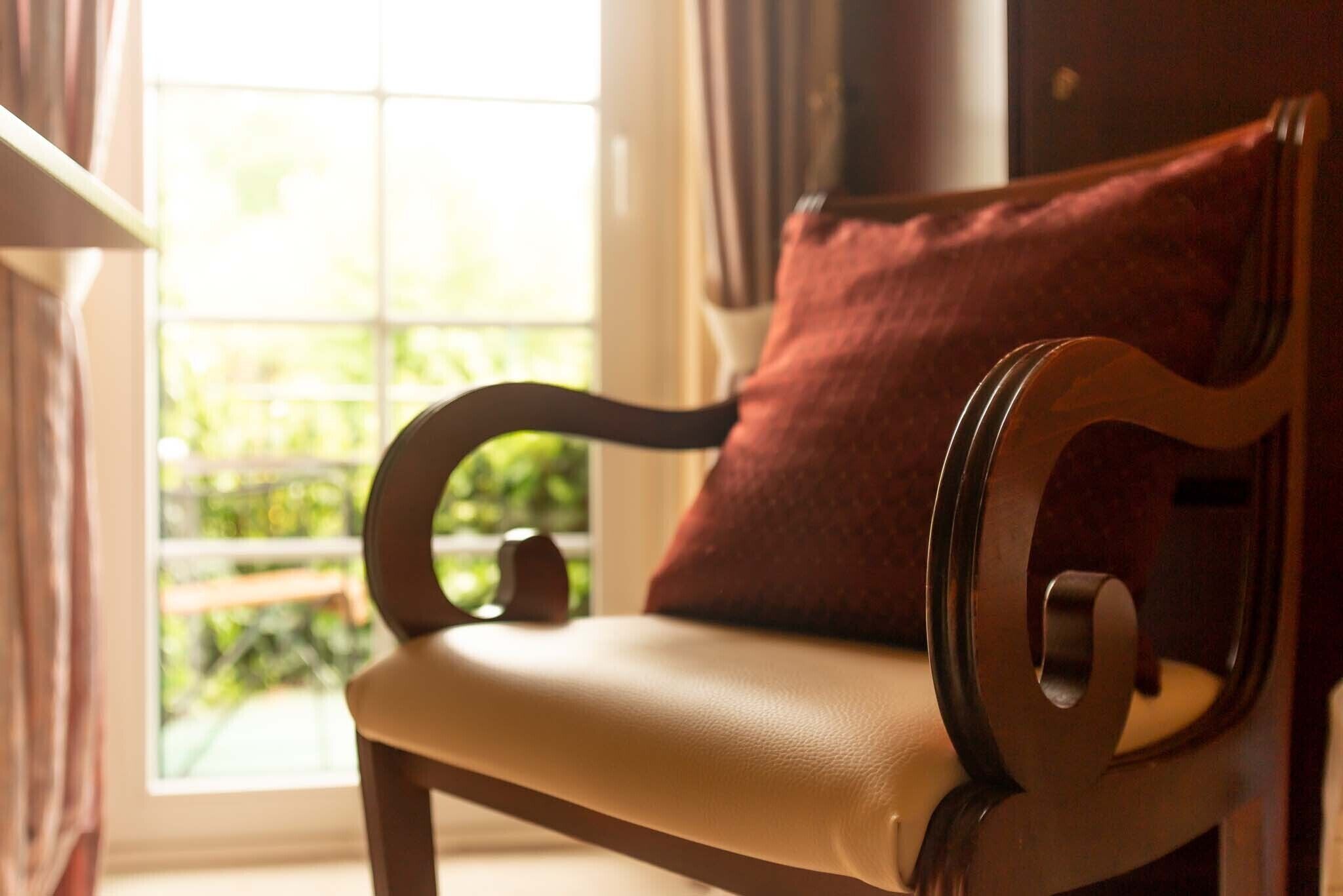 Une chaise en bois avec un coussin, placée près d’une fenêtre donnant sur un paysage verdoyant.