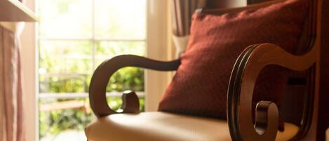 Une chaise en bois avec un coussin, placée près d’une fenêtre donnant sur un paysage verdoyant.